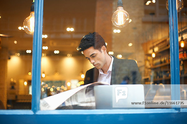Fensteransicht des Geschäftsmannes beim Lesen von Broadsheet-News im Cafe