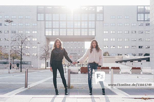 Portrait of twin sisters  in urban area  side by side  holding hands