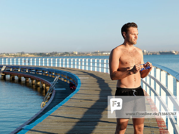 Swimmer holding swimming goggles on boardwalk  Eastern Beach  Geelong  Victoria  Australia