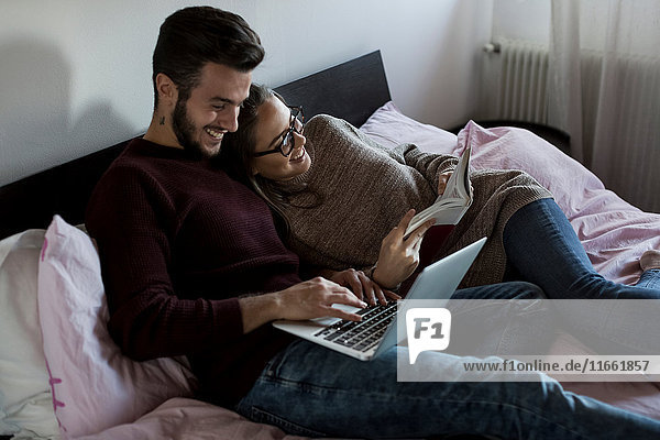 Young couple  relaxing on bed  young man using laptop  young woman reading book