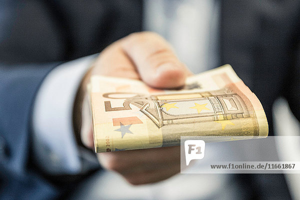 Close up of businessman's hand handing folded fifty euro notes