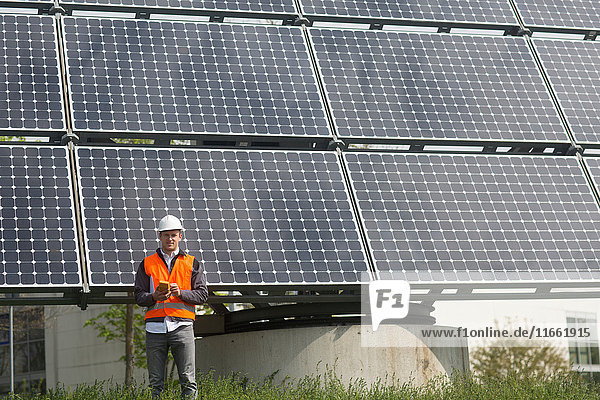 Porträt eines jungen männlichen Ingenieurs  der ein Multimeter am Standort eines Solarpanels hält