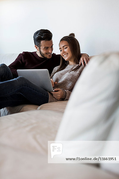 Young couple relaxing on sofa looking at laptop