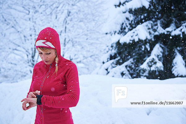 Läuferin in roter Kapuze kontrolliert Smartwatch im Schnee  Gstaad  Schweiz