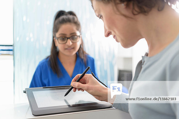 Dental receptionist assisting patient fill in form on digital tablet in dental surgery