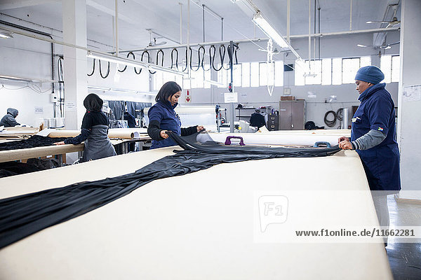 Fabrikarbeiter rollen Textilien auf Arbeitstisch in Bekleidungsfabrik aus