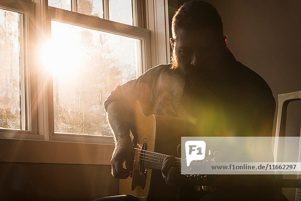 Mann spielt Gitarre neben dem Fenster