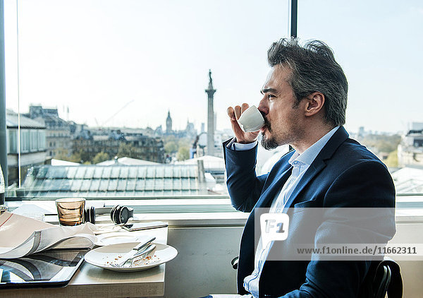 Geschäftsmann trinkt Kaffee am Restaurantfenster mit Blick auf die Dächer  London  UK