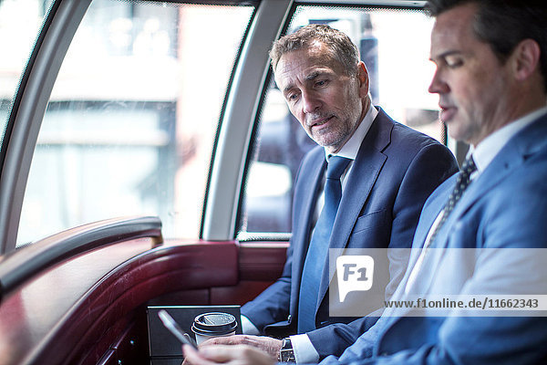 Zwei Geschäftsleute betrachten Smartphone im Doppeldeckerbus
