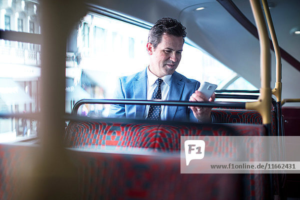 Geschäftsmann betrachtet Smartphone im Doppeldeckerbus