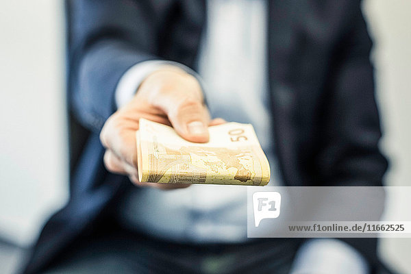 Businessman's hand handing folded fifty euro notes