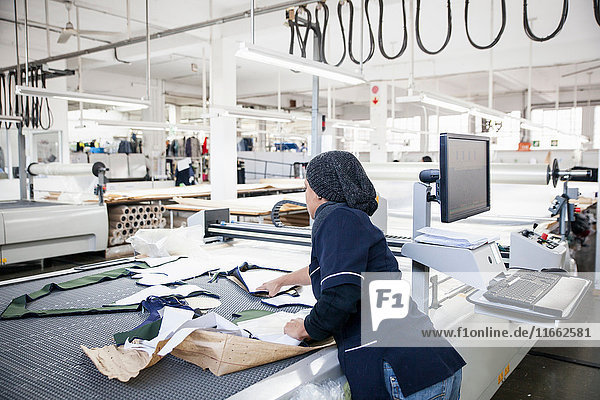 Fabrikarbeiter entfernt geschnittene Textilmuster von einer Musterschneidemaschine in einer Bekleidungsfabrik