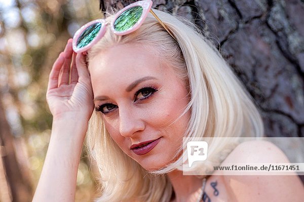 Portrait of a 30 year old blond woman looking at the camera  lifting large sunglasses on her head  outdoors.
