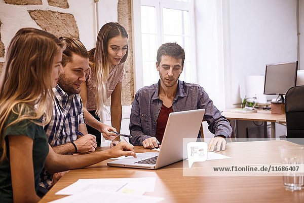 Young professionals in a conference room looking at a dedicated presentation on a laptop pc with interest and expectation with notepaper on the table.