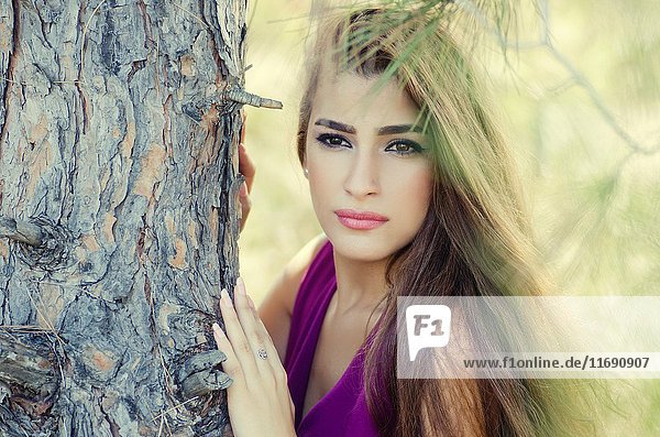Beautiful young woman leaning against a tree looking away.