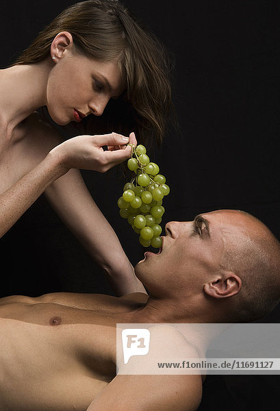 Nacktes Paar  Frau füttert Mann mit grünen Trauben.