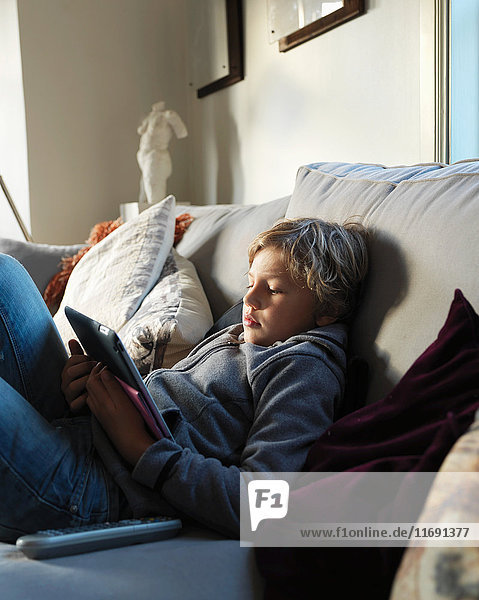 Teenage boy relaxing on sofa and using digital tablet