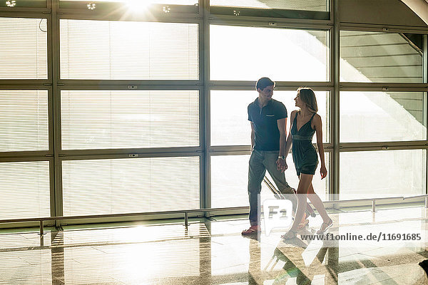 Young couple walking by window in sunlight in airport