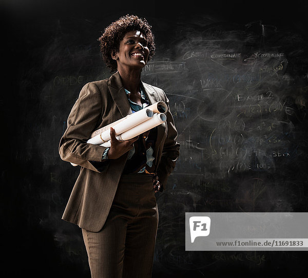Businesswoman holding blueprint by blackboard