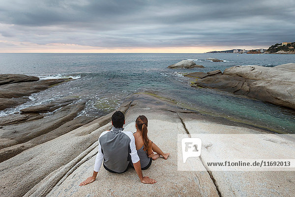 Ehepaar entspannt sich auf einem Felsblock am Meer