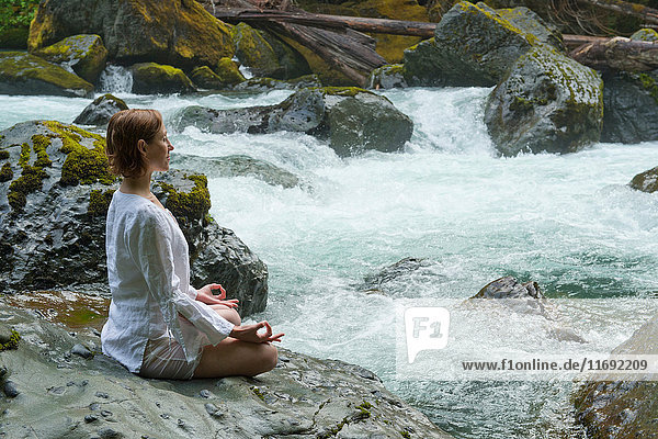 Frau meditiert auf Felsen am Wasser