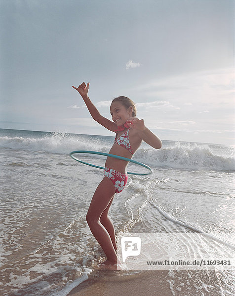Girl hula hooping in waves on beach