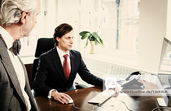Young businessman at desk with senior man in office