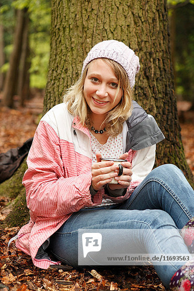 Lächelnde Frau trinkt Kaffee im Wald
