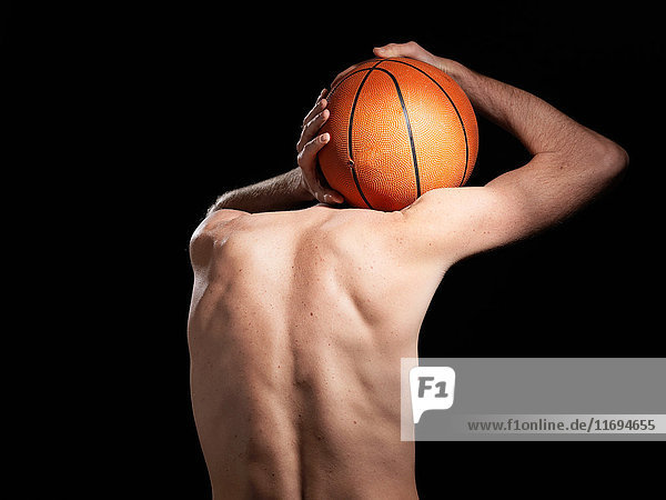 Rückansicht eines halb bekleideten Basketballspielers vor schwarzem Hintergrund