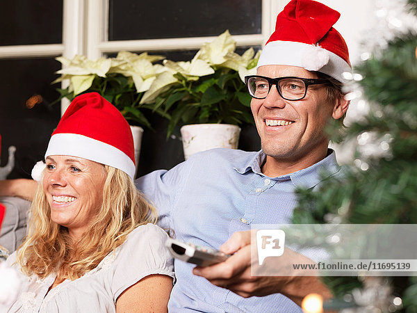 Erwachsenes Paar mit Weihnachtsmützen auf dem Sofa