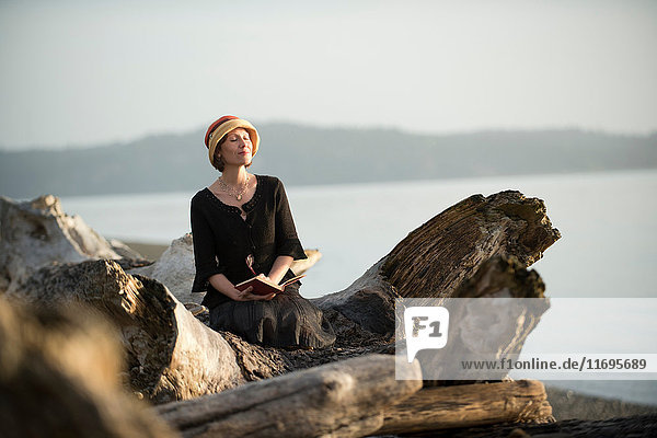 Frau sitzt auf Treibholz