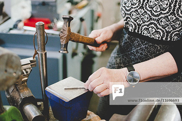 Mittelteil einer älteren Frau  die auf Metall hämmert  um in der Werkstatt Schmuck herzustellen.