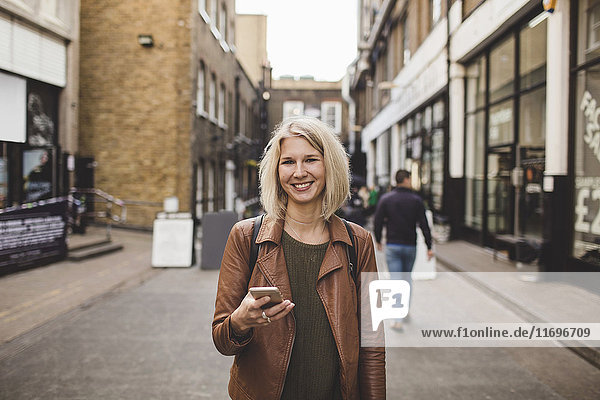 Porträt einer lächelnden jungen Frau mit Handy auf der Straße in der Stadt