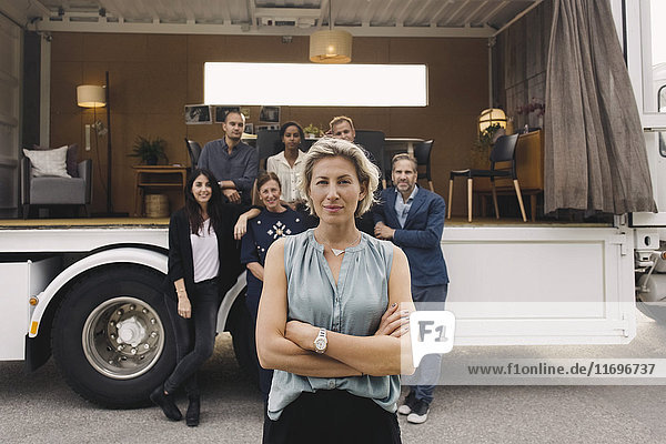 Porträt einer selbstbewussten Geschäftsfrau mit Team und tragbarem Bürotruck im Hintergrund