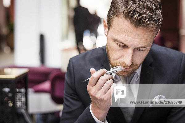 Mature businessman with pen in mouth sitting at hotel reception