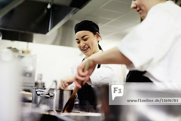 Smiling female chef student with colleague cooking food in commercial kitchen