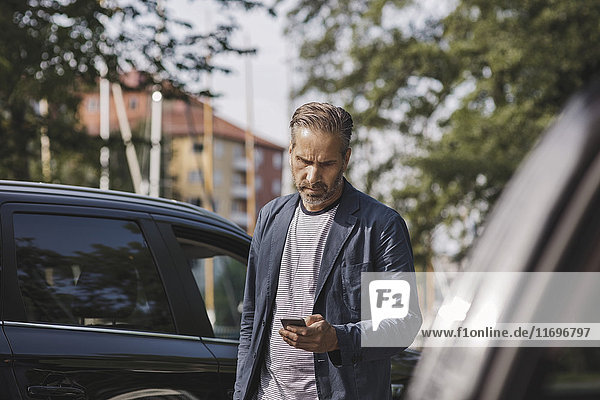 Businessman using smart phone while standing by cars at park
