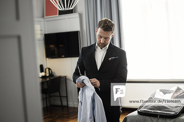 Erwachsener Mann hält Hemd in Kleiderbügel stehend im Hotelzimmer