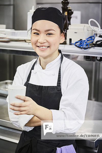 Porträt der lächelnden Köchin mit Einwegbecher in der Großküche