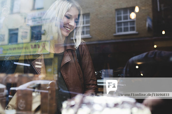 Smiling young woman wearing jacket in coffee shop seen through window