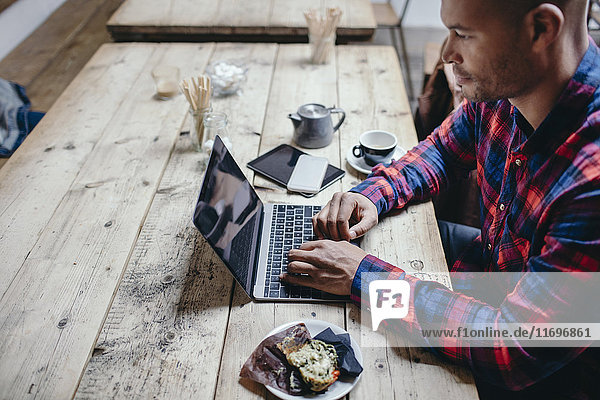 Seitenansicht eines erwachsenen Mannes mit Laptop am Tisch im Coffee Shop