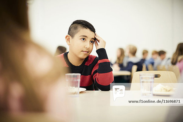 Nachdenklicher Junge bei Tisch in der Mittagspause in der Schulcafeteria