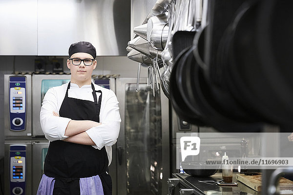 Porträt eines männlichen Kochstudenten  der in der Großküche gekreuzt steht.