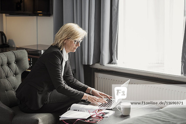 Seitenansicht der Geschäftsfrau mit Laptop am Fenster im Hotelzimmer