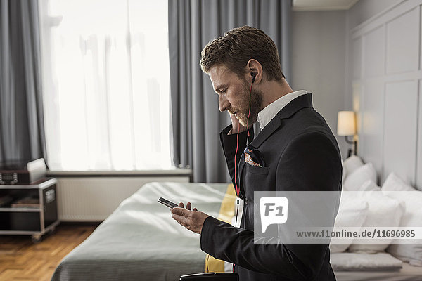 Seitenansicht des Geschäftsmannes beim Abhören des Handys im Hotelzimmer