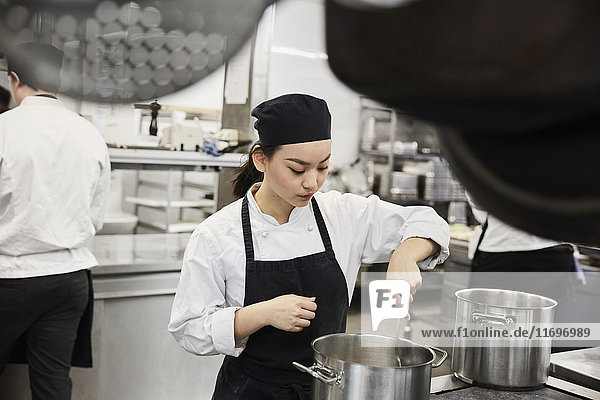 Young female chef stirring food in cooking pan at commercial kitchen