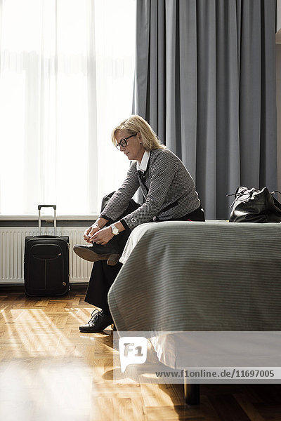 Seitenansicht der Geschäftsfrau beim Schnürsenkelbinden auf dem Bett im Hotelzimmer