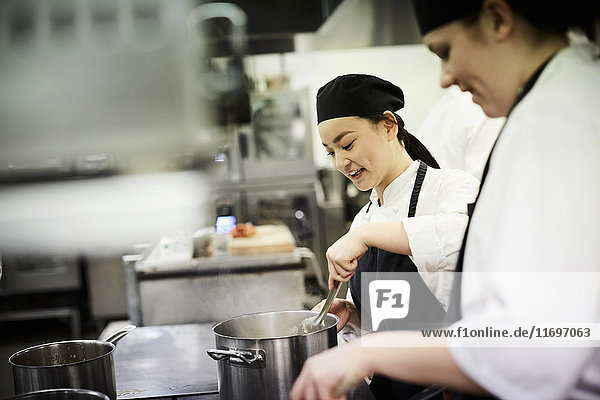 Female chef student with colleague cooking food in commercial kitchen