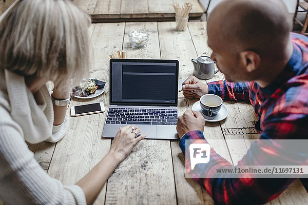 Multi-ethnic couple using laptop at table in coffee shop