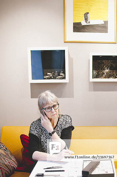Seniorin mit Handy am Schreibtisch in der Schmuckwerkstatt